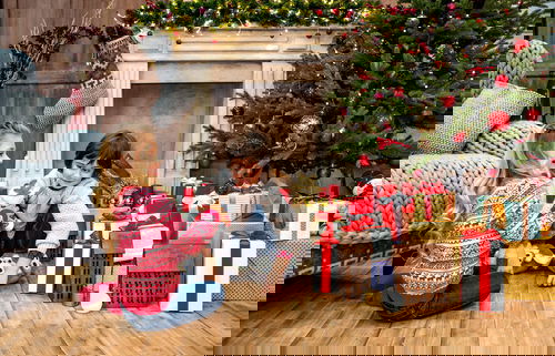 A young girl and boy opening presents under the Christmas tree fireplace with stockings hung