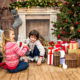 A young girl and boy opening presents under the Christmas tree fireplace with stockings hung