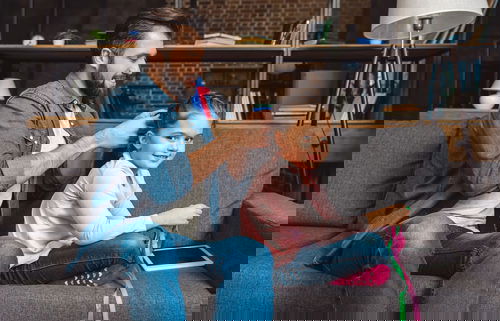 smiling father braiding his smiling daughters hair on the sofa as she plays with ribbons