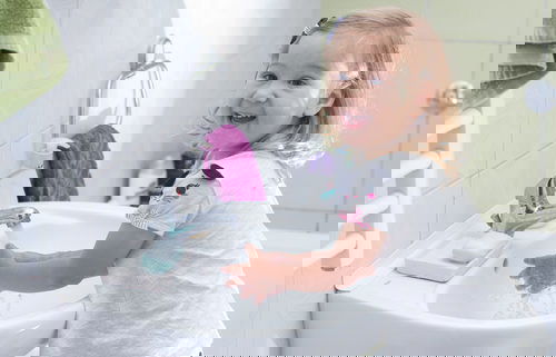 smiling happy toddler washing her hands at a bathroom sink