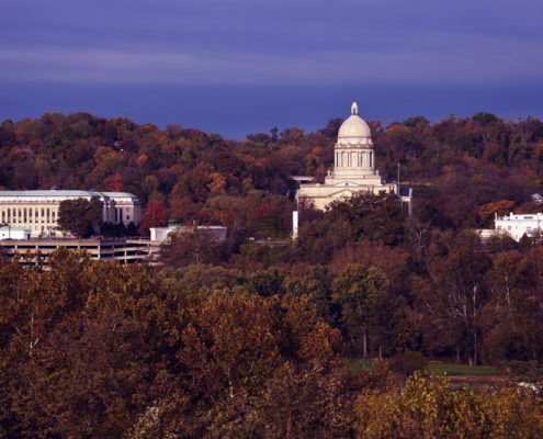A distant shot of the FrankFort Kentucky State Capitol building and Governor's mansion with a blue sky in the background and fall trees all around