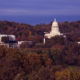 A distant shot of the FrankFort Kentucky State Capitol building and Governor's mansion with a blue sky in the background and fall trees all around