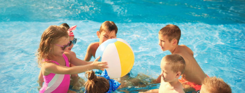 young kids playing with a beach ball in the pool
