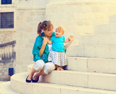 smiling mom holding her smiling toddler on the steps of an old brick building