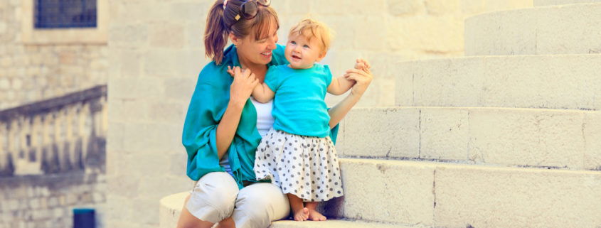 smiling mom holding her smiling toddler on the steps of an old brick building