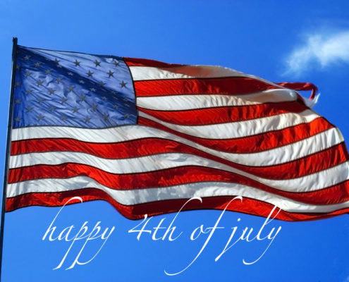 American flag waving in the wind with a bright blue sky in the background happy 4th of July written in white italics under the flag