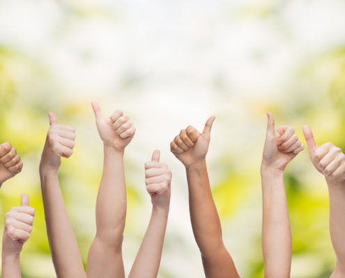 Bunch of arms raised in the air making the thumbs up with trees in the background
