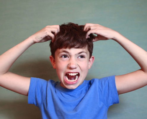 Young boy is upset he needs a head check because he may have lice wearing a blue t-shirt