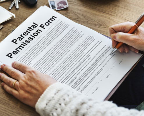 picture of a parental permission form on a desk in front of a mother holding a pen ready to sign the form