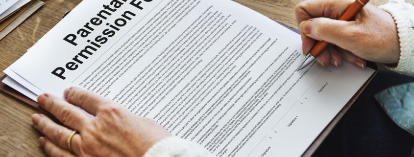 picture of a parental permission form on a desk in front of a mother holding a pen ready to sign the form