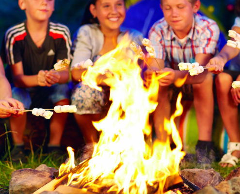 Kids smiling and roasting marshmallows around a campfire at summer camp
