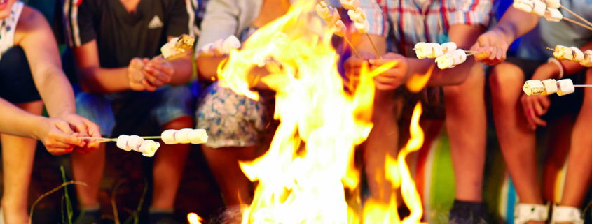 Kids smiling and roasting marshmallows around a campfire at summer camp