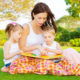 Image of cute young female with two little children read book outdoors, brother and sister with mother learning in the park in spring time, preschool education, day care, happy family concept